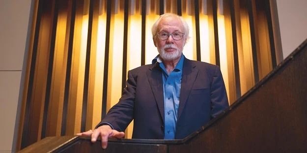 Bob standing beside a staircase, wearing a blazer and blue shirt